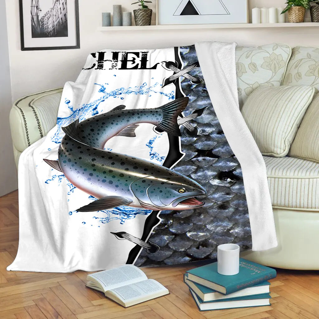 Plaid saumonier personnalisé motif écailles bleu marine et prénom, posé sur canapé clair, ambiance halieutique premium