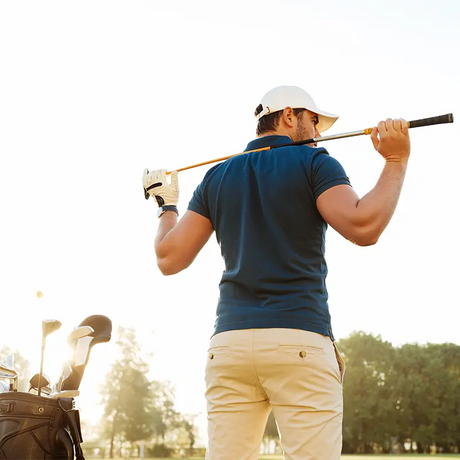 Golfeur en plein follow-through sur fairway à l'aube, polo personnalisé logo club, drapeau du green au loin